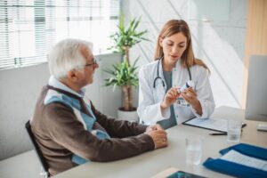 A doctor holding a medication bottle meets with an older male patient