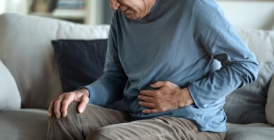 Man sitting on a couch, holding his stomach in discomfort