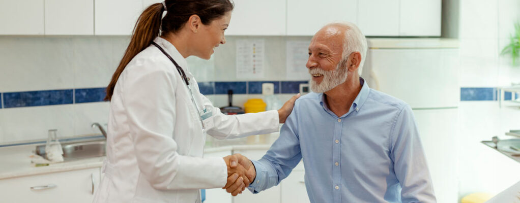 A doctor shakes a male patient's hand and pats him on the shoulder with her other hand