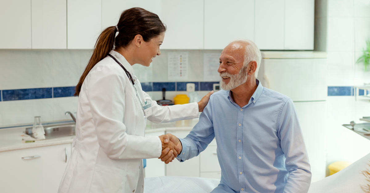 A doctor shakes a male patient's hand and pats him on the shoulder with her other hand