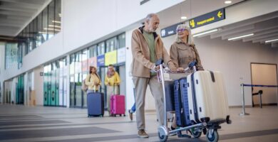 An older man and woman walk through an airport with a luggage cart