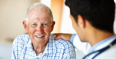 A doctor reassures an older man who's smiling into the camera.