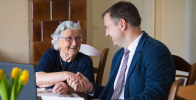 An older woman shakes hands with a lawyer sitting at her kitchen table