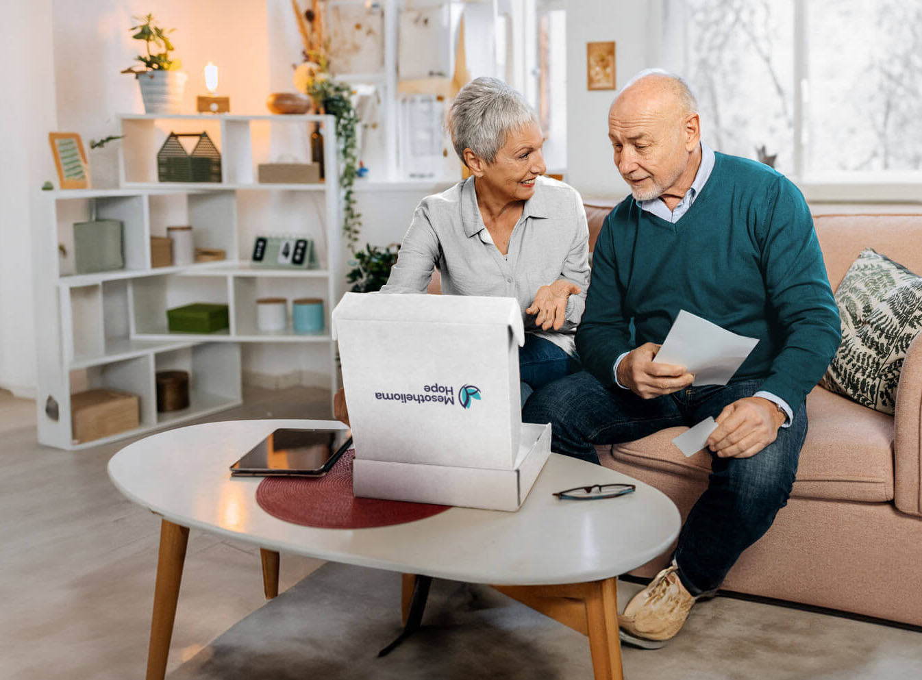 A husband and wife sit on a couch opening their Mesothelioma Hope care package